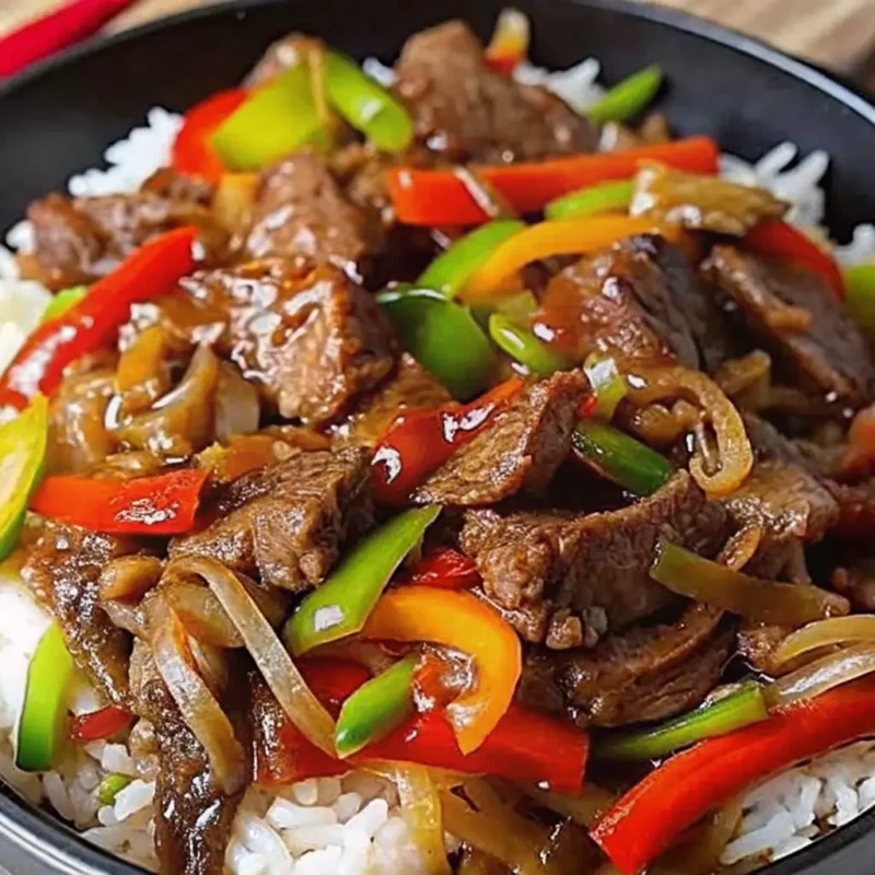 a mouth-watering image of a beef stir fry with white rice and green and red peppers, and onion