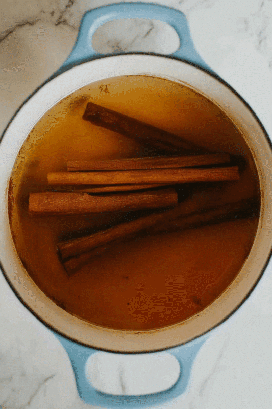 A turquoise enameled Dutch oven filled with hot water and whole cinnamon sticks, steeping to make authentic Mexican Cinnamon Tea (Té de Canela). The rich, amber-colored liquid is infused with aromatic canela, capturing the essence of a traditional herbal remedy