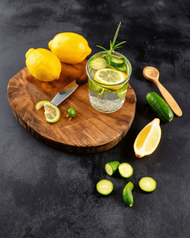 "Refreshing cucumber lemon water in a tall glass with ice, lemon slices, cucumber rounds, and mint leaves, garnished with a striped straw."
