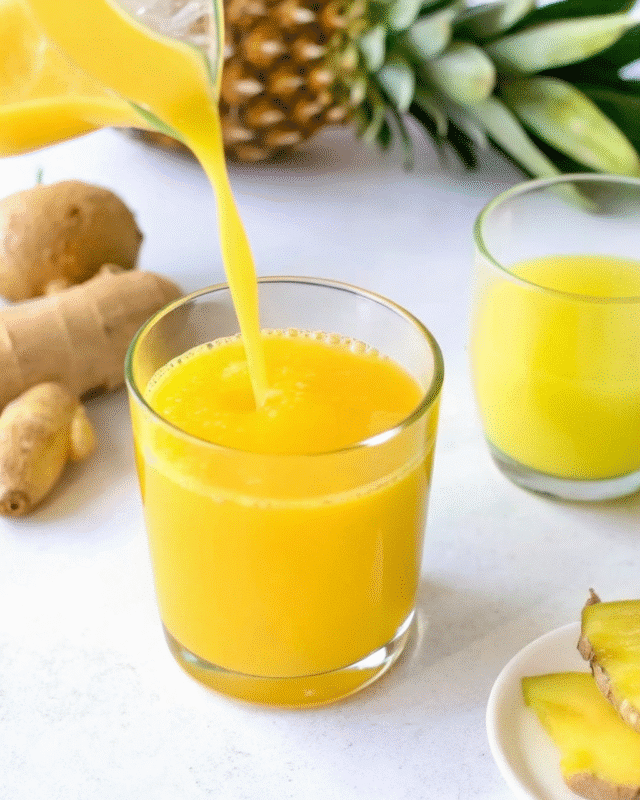 A vibrant yellow pineapple ginger juice is being poured into a glass, with fresh pineapple slices and ginger roots in the background.